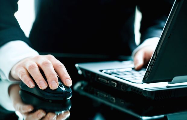 Hands on a laptop keyboard and a mouse at a dark desk