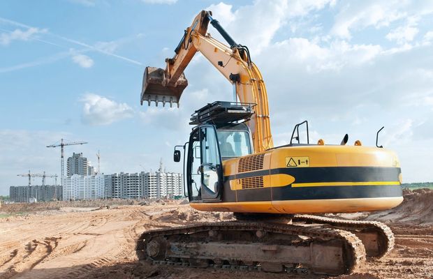 A tracked excavator on a building site with cranes behind it
