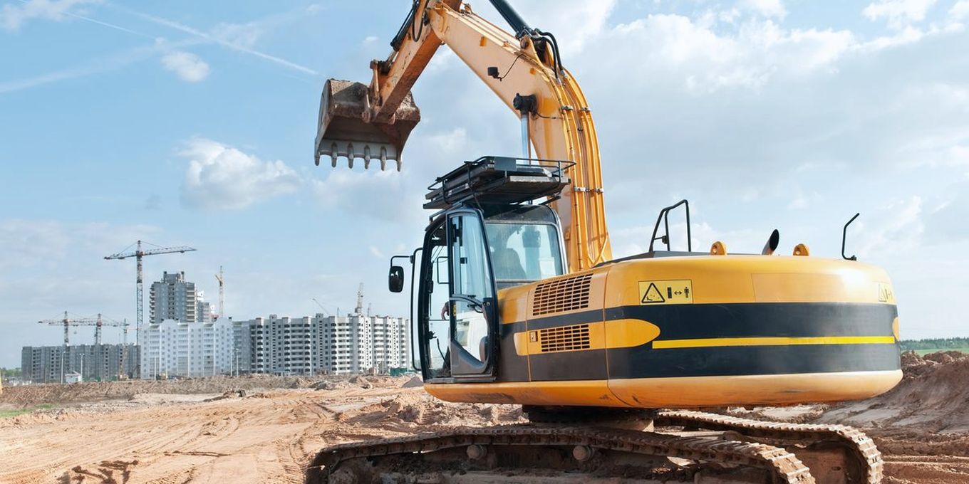 A tracked excavator on a building site with cranes behind it