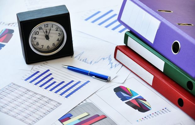 A desk clock beside binders and printed bar charts
