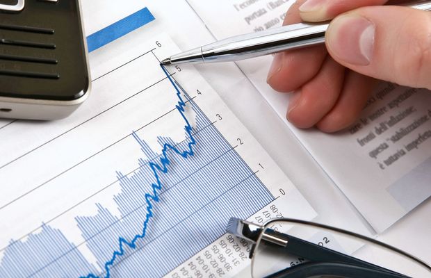 A hand with a pen points at the peak of a line on a printed market chart